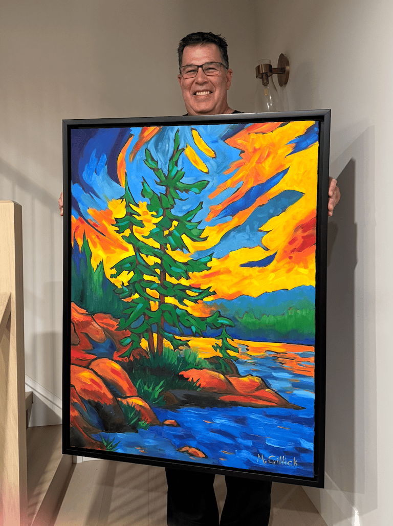 Mitch Gillick holding a painting of a Muskoka sunset