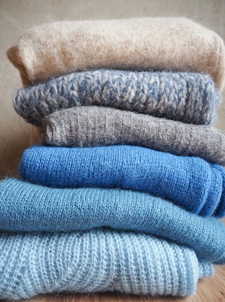 szare i niebieskie swetry ułożone w stos na tle szarej ściany