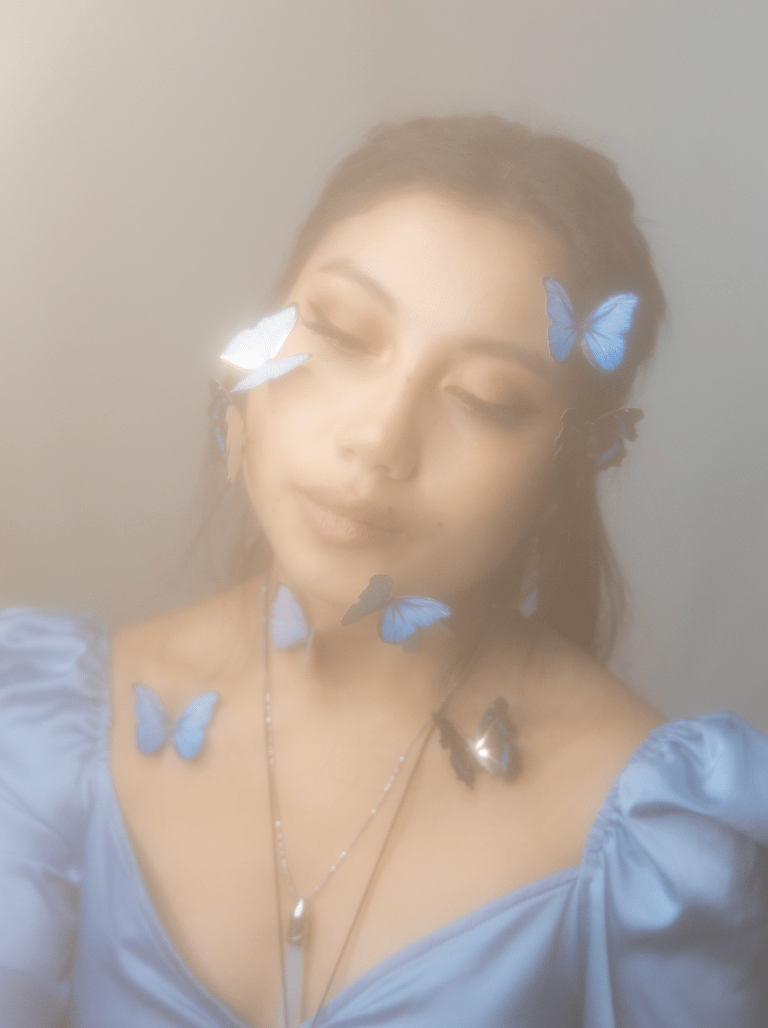 A dreamy and hazy self portrait of a young adult Asian woman, blue butterflies on face and neck