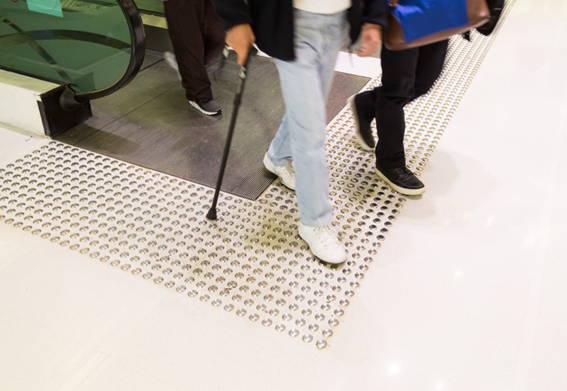 saida de escada rolante com piso tatil de alerta e pessoa com bengala circulando