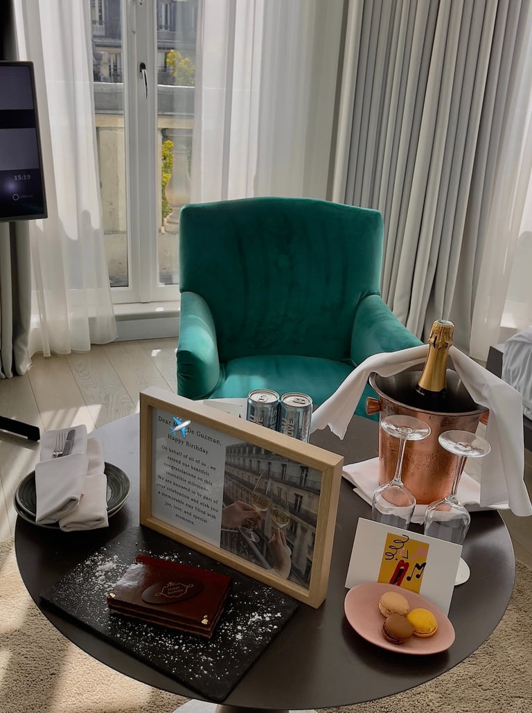 a table with a bottle of champagne, card, cake, macaroons, dessert, and framed letter
