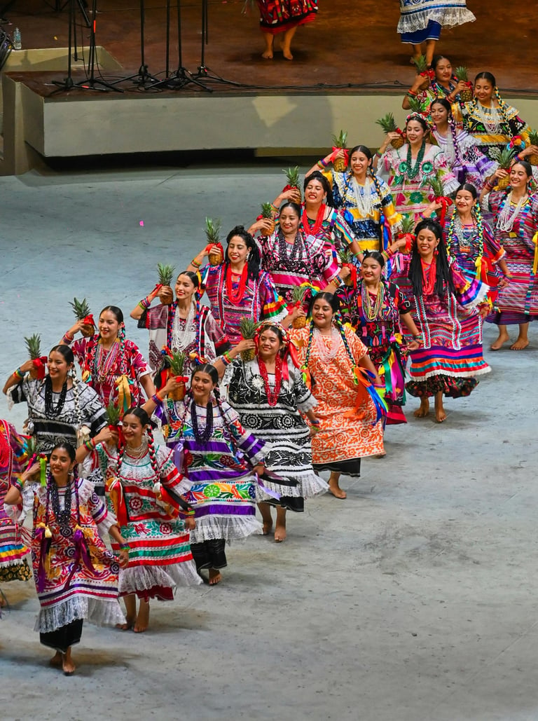 Mujeres bailando Flor de Piña con huipiles y piñas en la Guelaguetza, Oaxaca