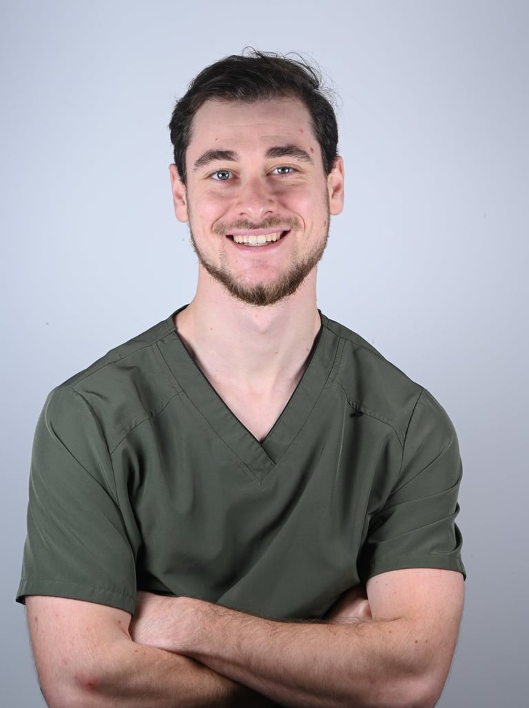 A smiling male healthcare professional wearing olive green medical scrubs with arms crossed.
