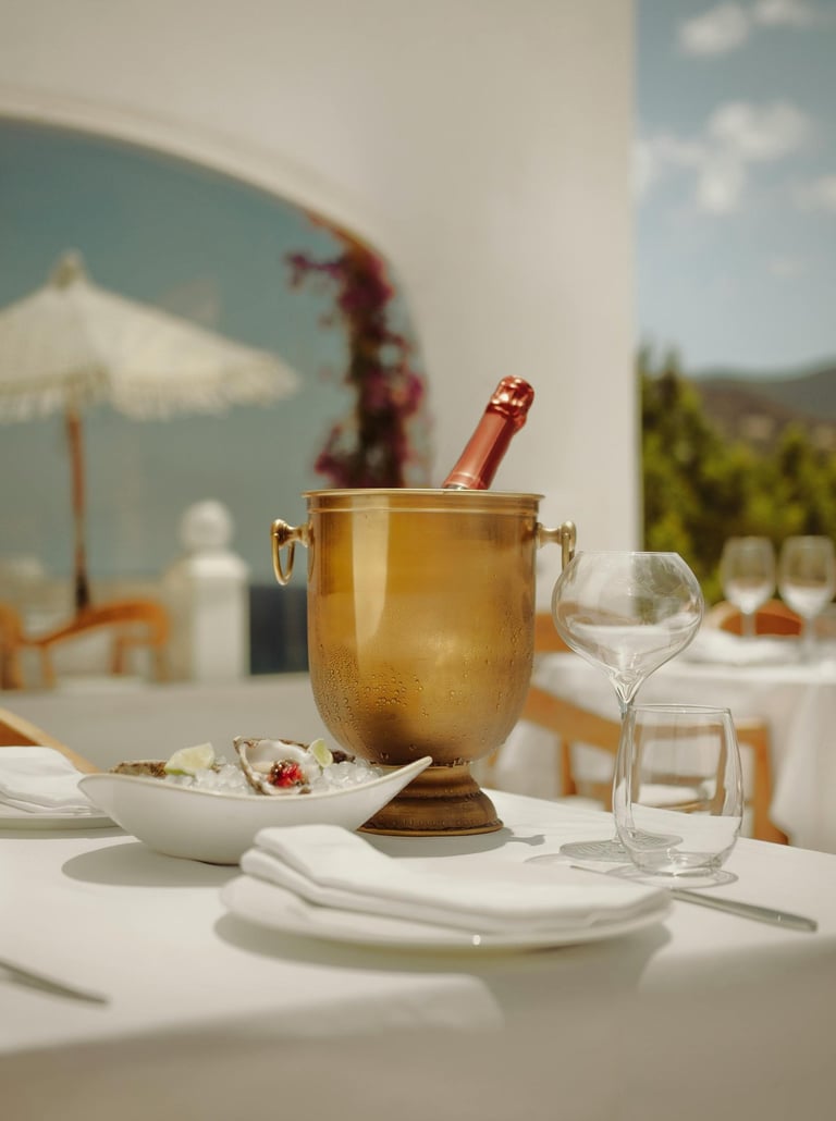 Outdoor dining table with champagne in an ice bucket, oysters on a plate, and empty glasses.