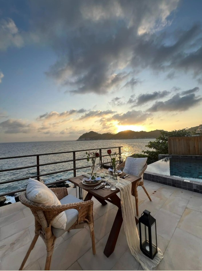 A romantic sunset dinner table set for two on a private oceanfront balcony with an infinity pool.