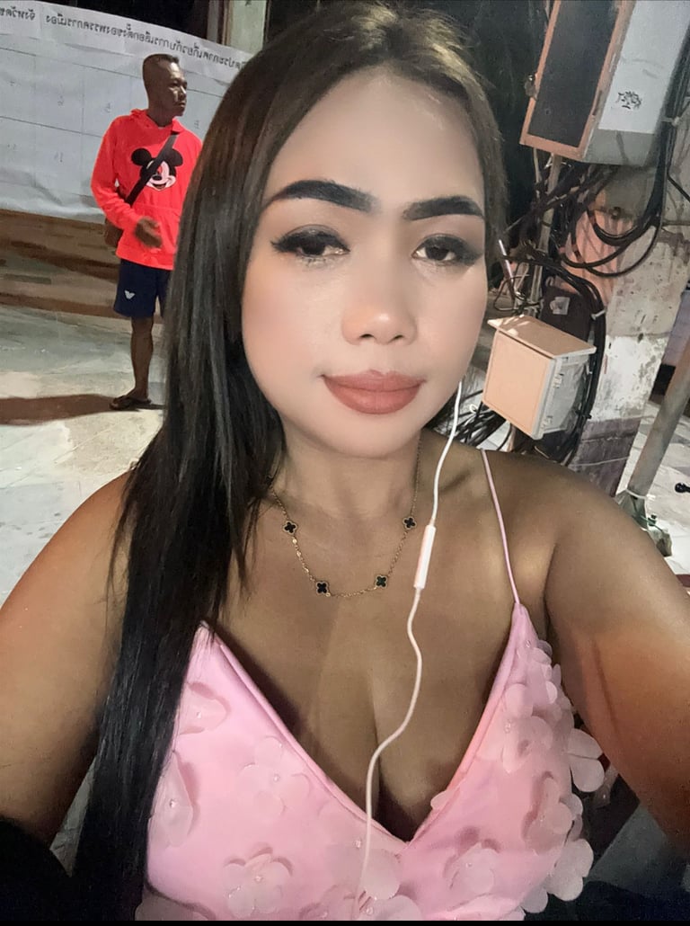 Lady wearing a pink top with headphones in left ear and a man standing in the background