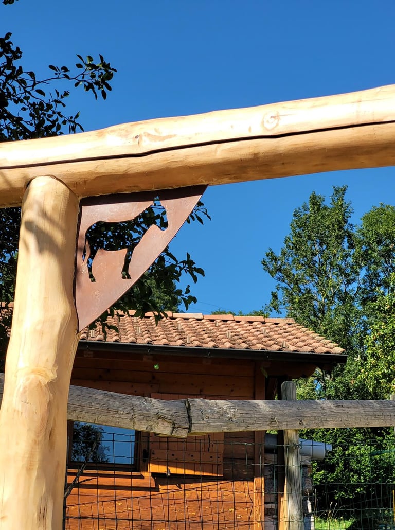 Rustic log fence post with a decorative donkey metal cutout on a farm under a blue sky.