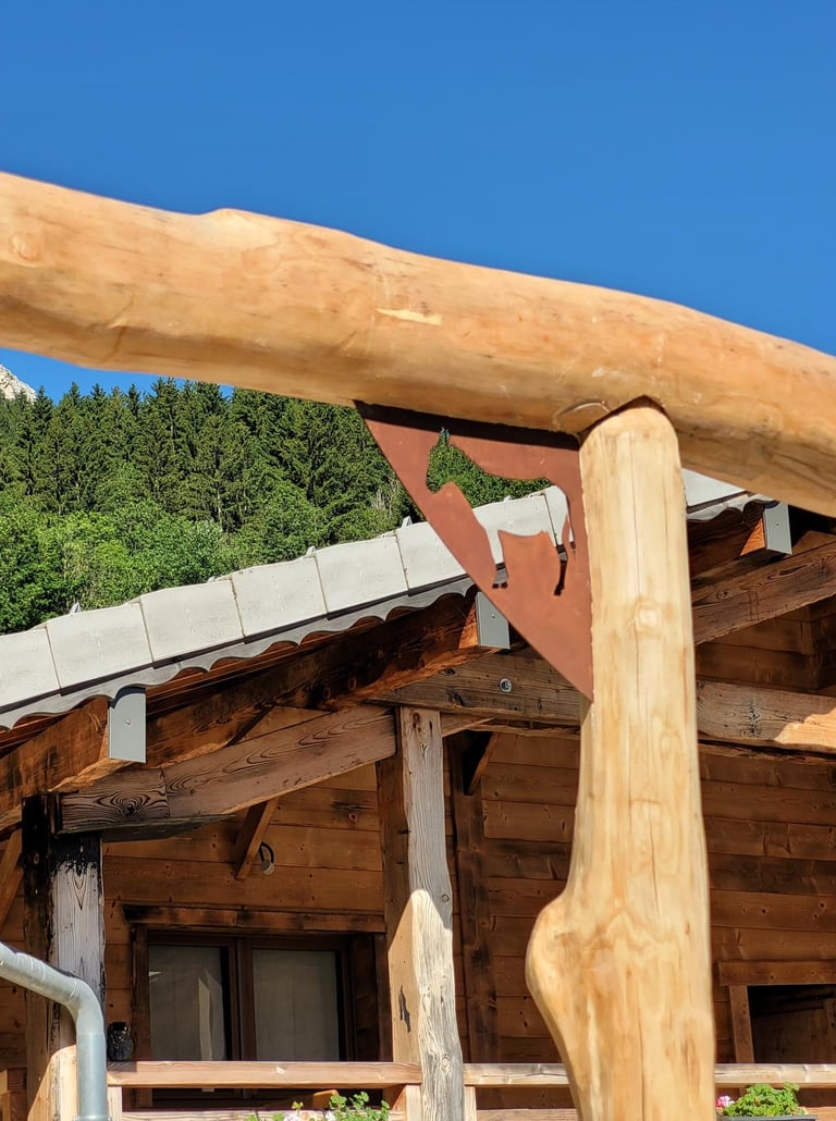 Rustic wooden alpine chalet featuring a decorative metal cow silhouette bracket against a clear blue sky.