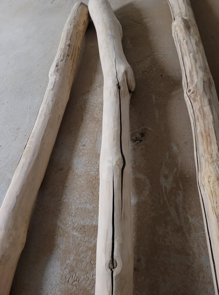 Three natural peeled log posts resting on a concrete floor for rustic construction.