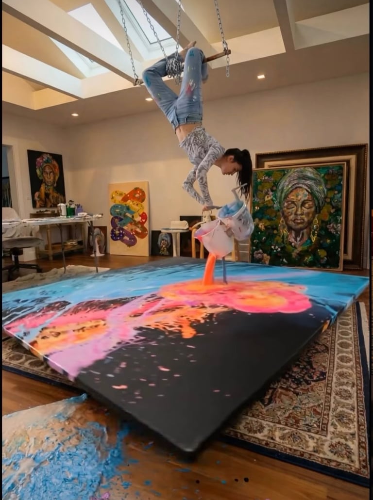 Aerial artist pours vibrant acrylic paint onto a large canvas while hanging upside down in an art studio.