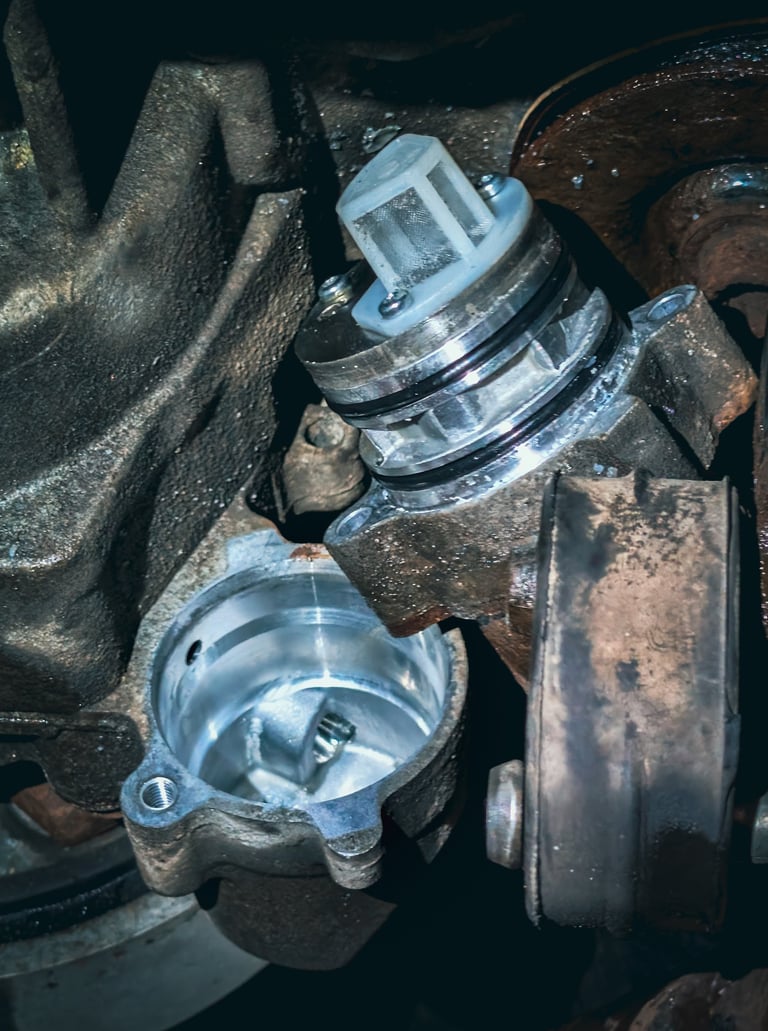 Close-up of a clean car oil pump screen and filter assembly being installed into a greasy engine housing.