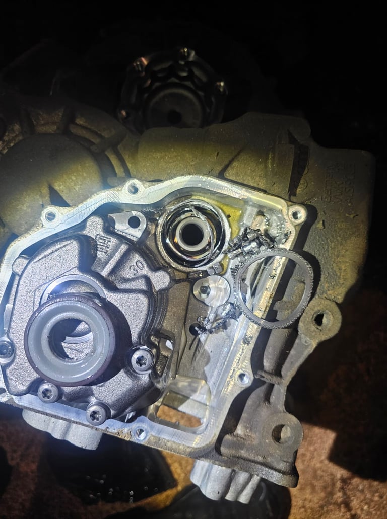 Damaged car transmission housing showing broken metal shards and mechanical failure inside the gearbox.