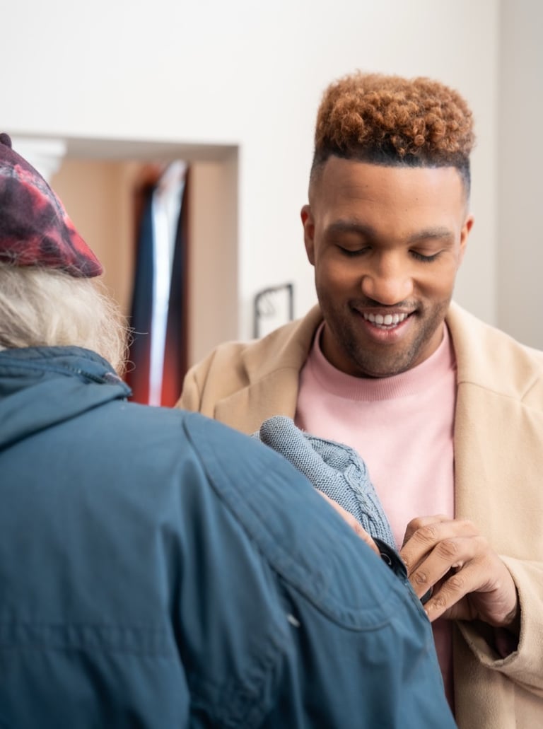 A male caregiver helps a male elderly client put on gloves