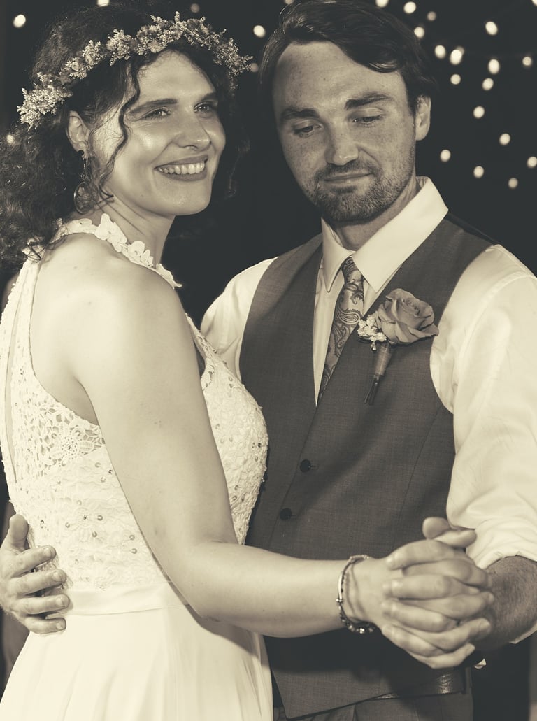a bride and groom dancing at a wedding reception in a barn with lights