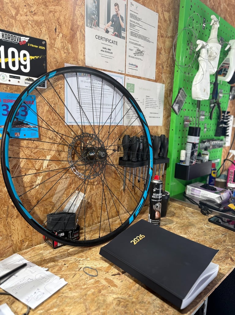 Mountain bike wheel with blue rim tape on a wooden workbench in a bicycle repair shop.