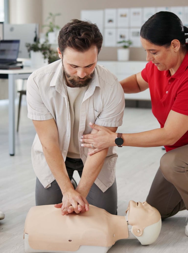 Female instructor assisting a male student learning how to perform CPR on a training mannequin
