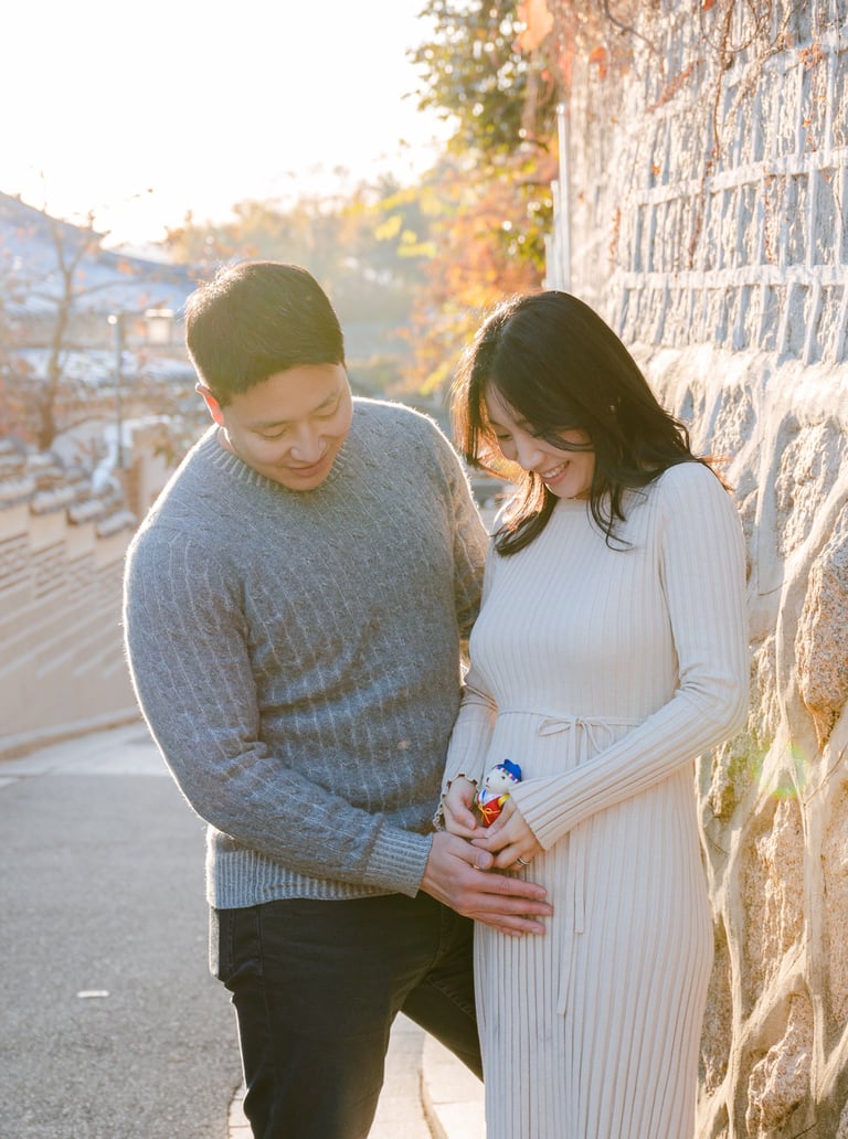 a pregnant woman and her husband are standing next to a stone wall