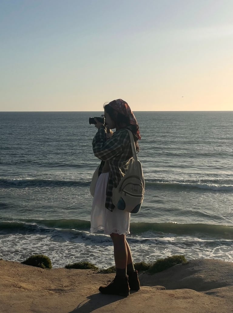 Vibey full body candid shot of me holding camera up to my face, standing on cliffs over ocean.Earthy