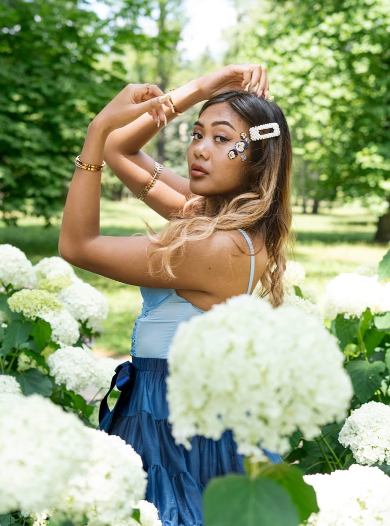 Portrait photo of a young Indonesian woman in a park with flowers and whimsical blue dress