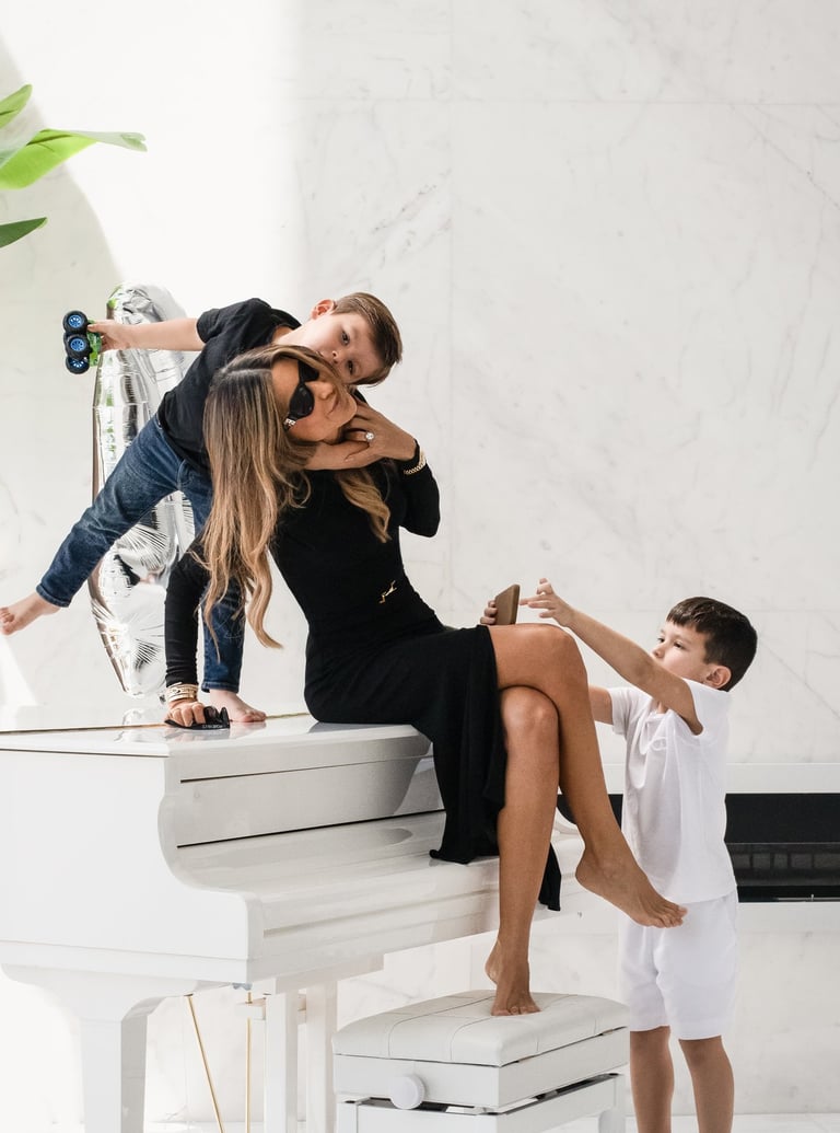 Mother in black dress playing with her two sons on a white piano.