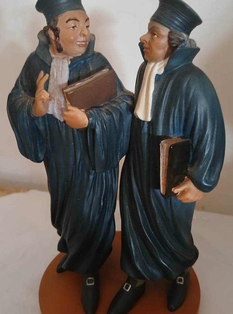 Statue vintage de deux avocats en robe traditionnelle et chapeau portant des dossiers juridiques.