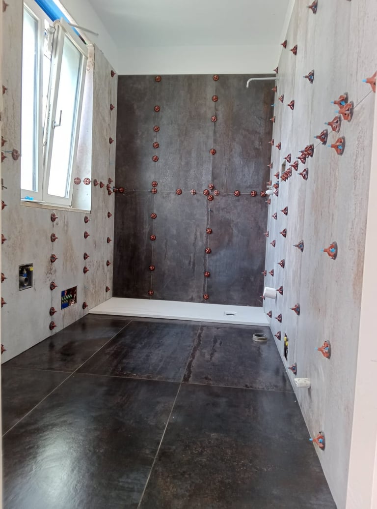 Bathroom renovation featuring dark floor tiles and wall tiling with red leveling spacers.