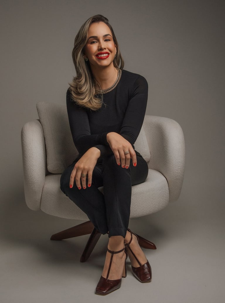 Professional woman in elegant black attire sitting in a modern chair for a corporate studio portrait.