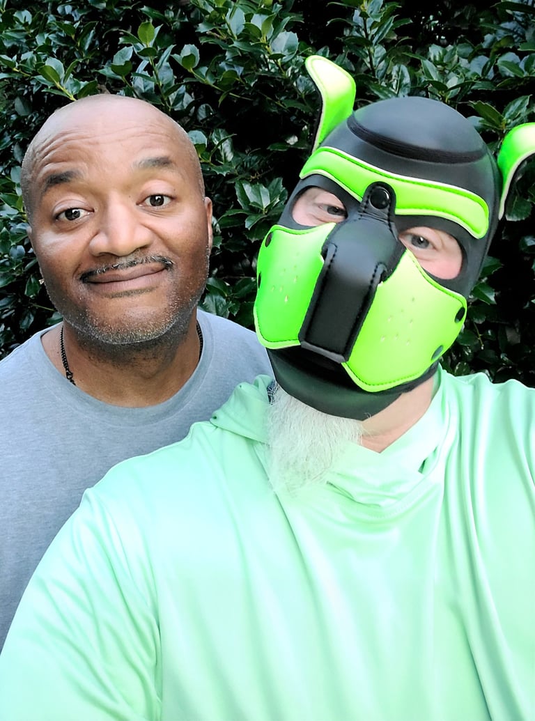 2 Men, 1 wearing a pup mask, posing together.
