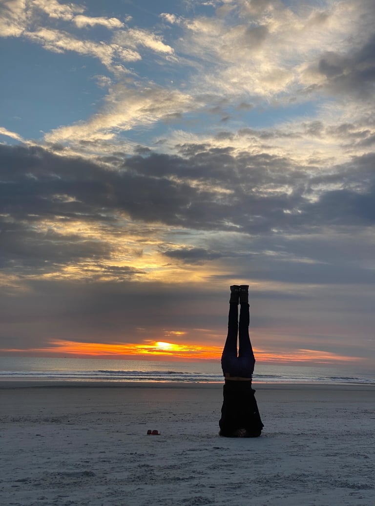 A woman doing a headstand on the beach silhouetted by the sunrise