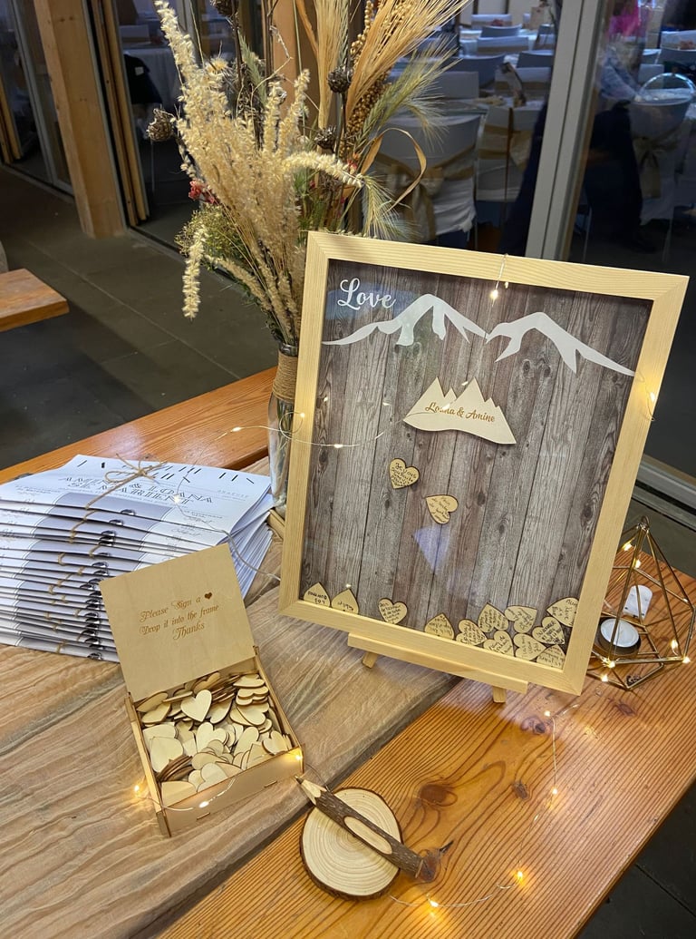 Rustic wedding guest book display featuring a mountain shadow box frame with wooden heart tokens.