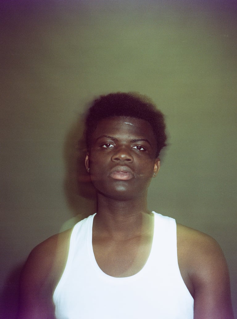 Film portrait of a young Black man in a white tank top with aesthetic grain and lens flare.