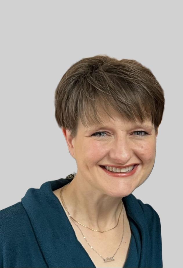 Professional headshot of a smiling woman with short brown hair and a blue sweater on a grey background.