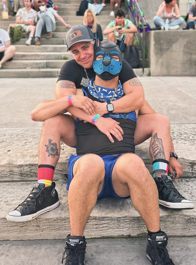 Two men, one wearing a pup mask, pose together.