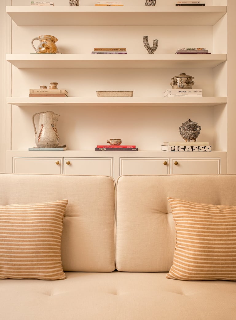 Bibliothèque sur mesure avec objets d’art et canapé clair dans un salon haussmannien rénové à Paris