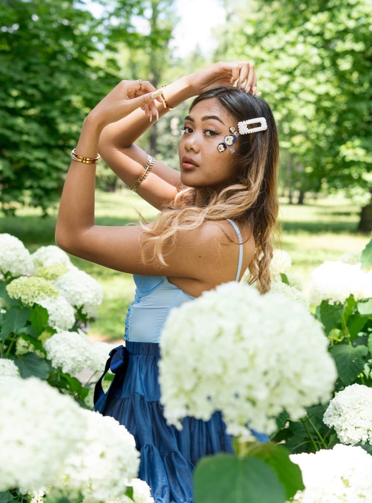 Portrait photo of a young Indonesian woman in a park with flowers and whimsical blue dress