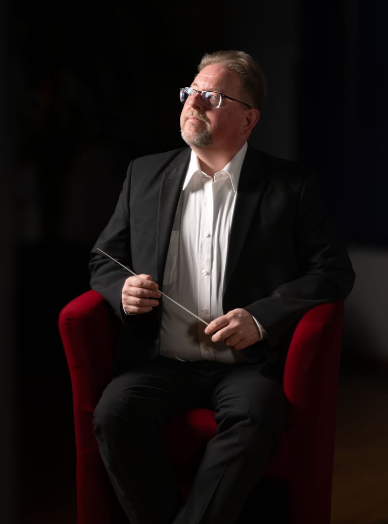 Robert in a suit and tie is holding a conductor's baton