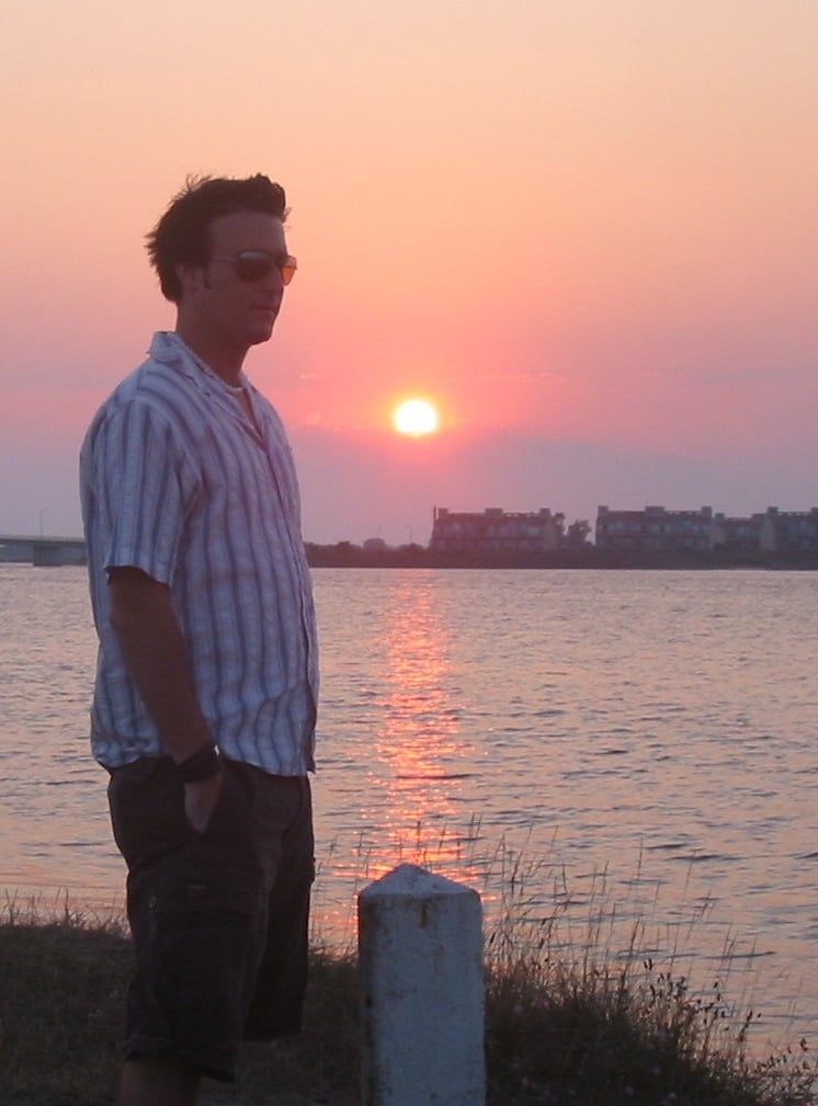 A man standing in front of the ocean with a sunset