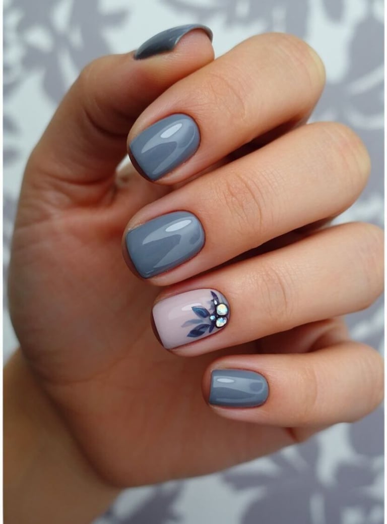 Dusty blue-grey fall nails with navy leaf accents and crystal embellishments.
