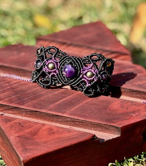Pulsera de macramé artesanal en negro y morado con amatistas, exhibida sobre un soporte de madera.