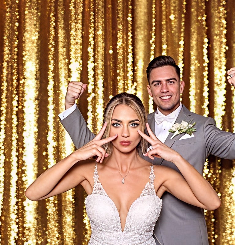 ein Hochzeitspaar aus Pforzheim steht vor der Fotobox vor einem gold glänzendem Hintergrund