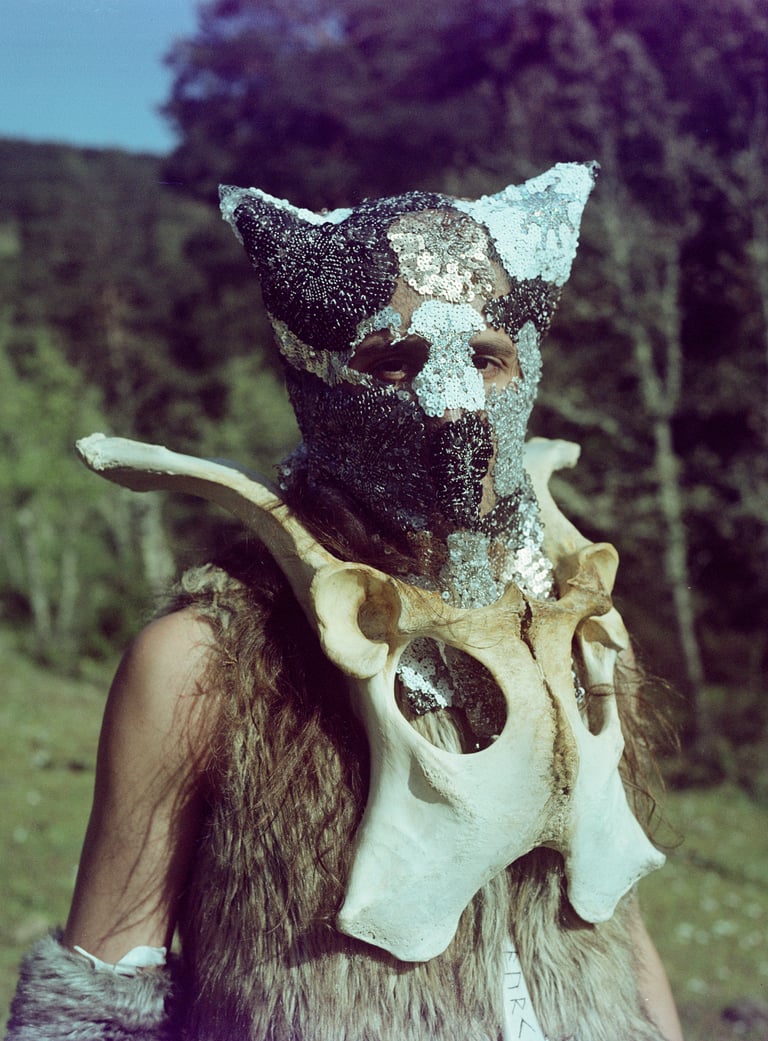 A person wearing a beaded animal mask and a large bone collar in a shamanic ritual style costume.