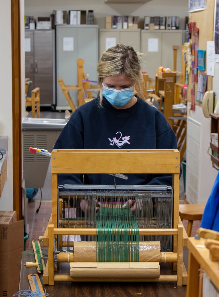 Someone standing behind a table loom adjusting her piece.