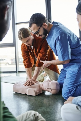 A male nurse teaching a man to administer first aid CPR on a dummy