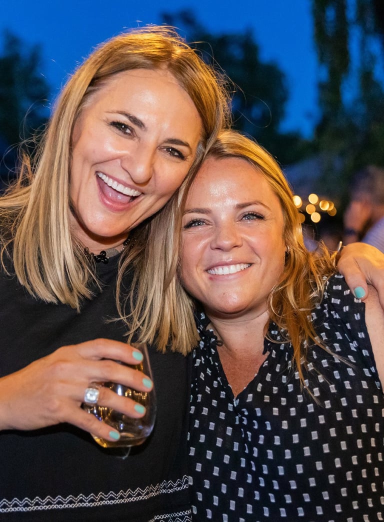 two women hugging for a photo at a party. Their faces are filled with warmth