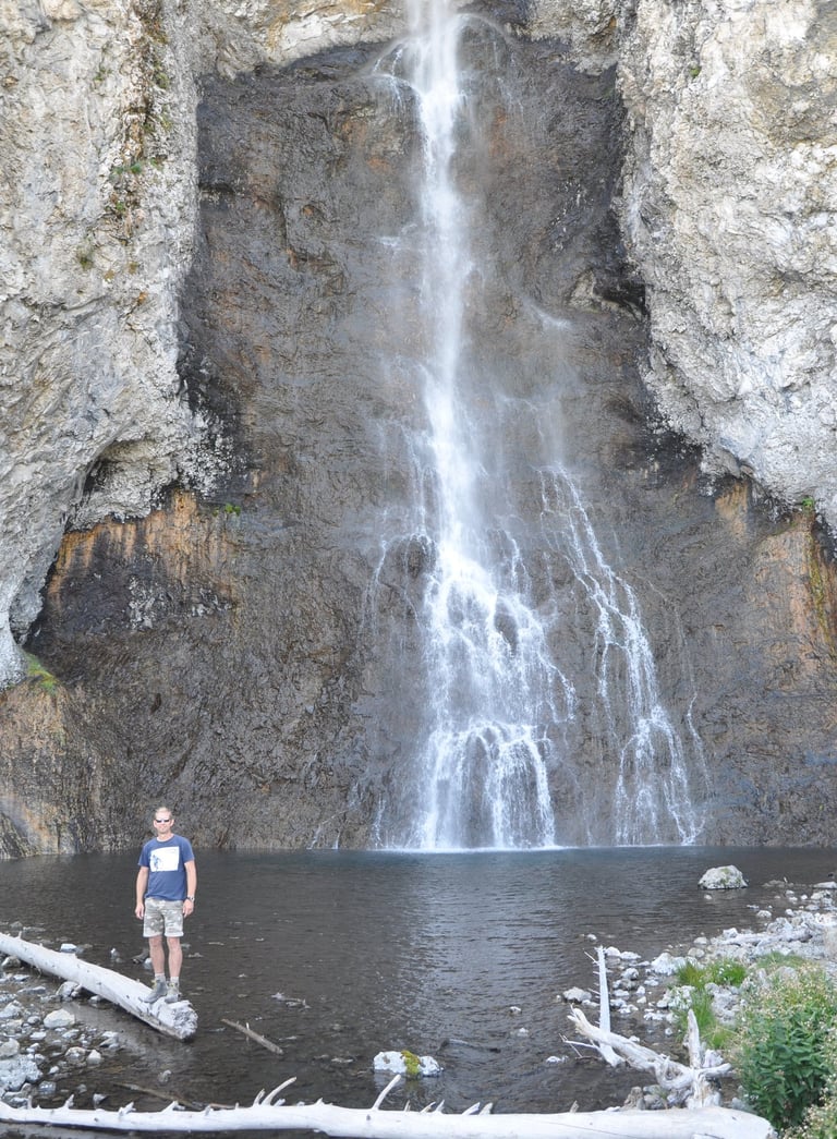 a man standing in front of Fairy Falls waterfall in Yellowstone National Park