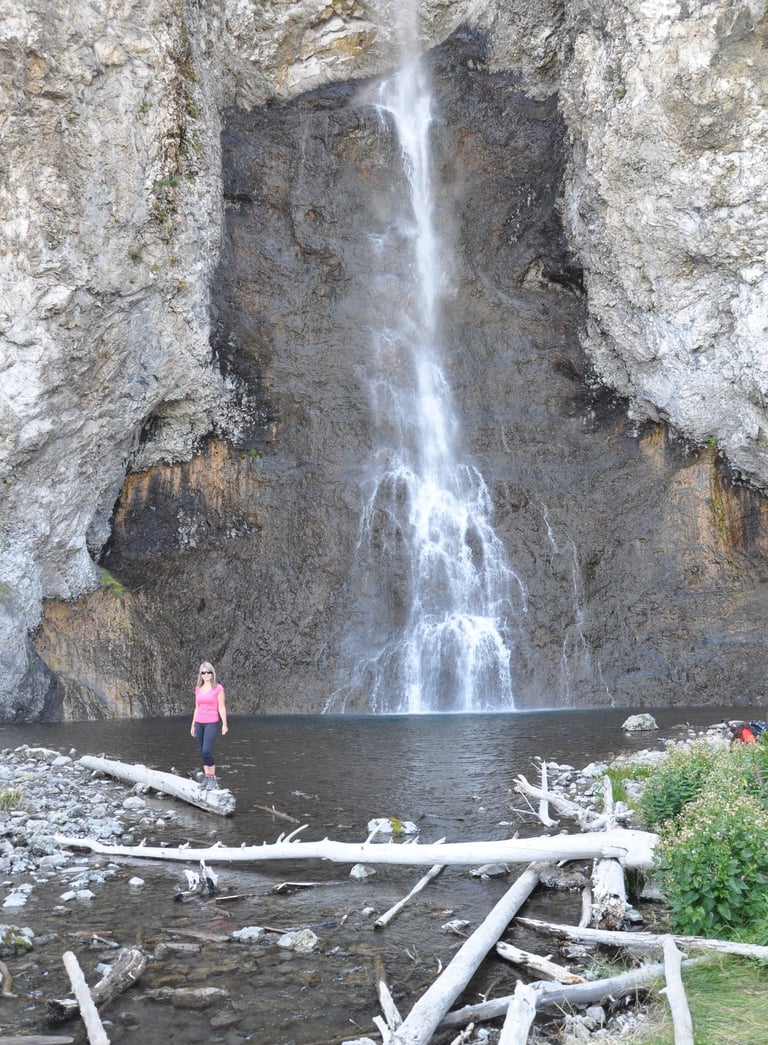 a woman standing in front of Fairy Falls waterfall in Yellowstone National Park