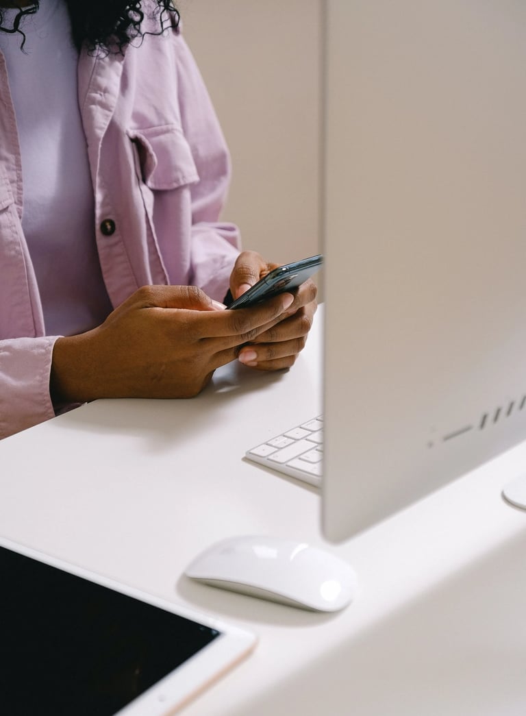 Femme brune, assise à son bureau, qui pianote sur son téléphone portable devant son ordinateur