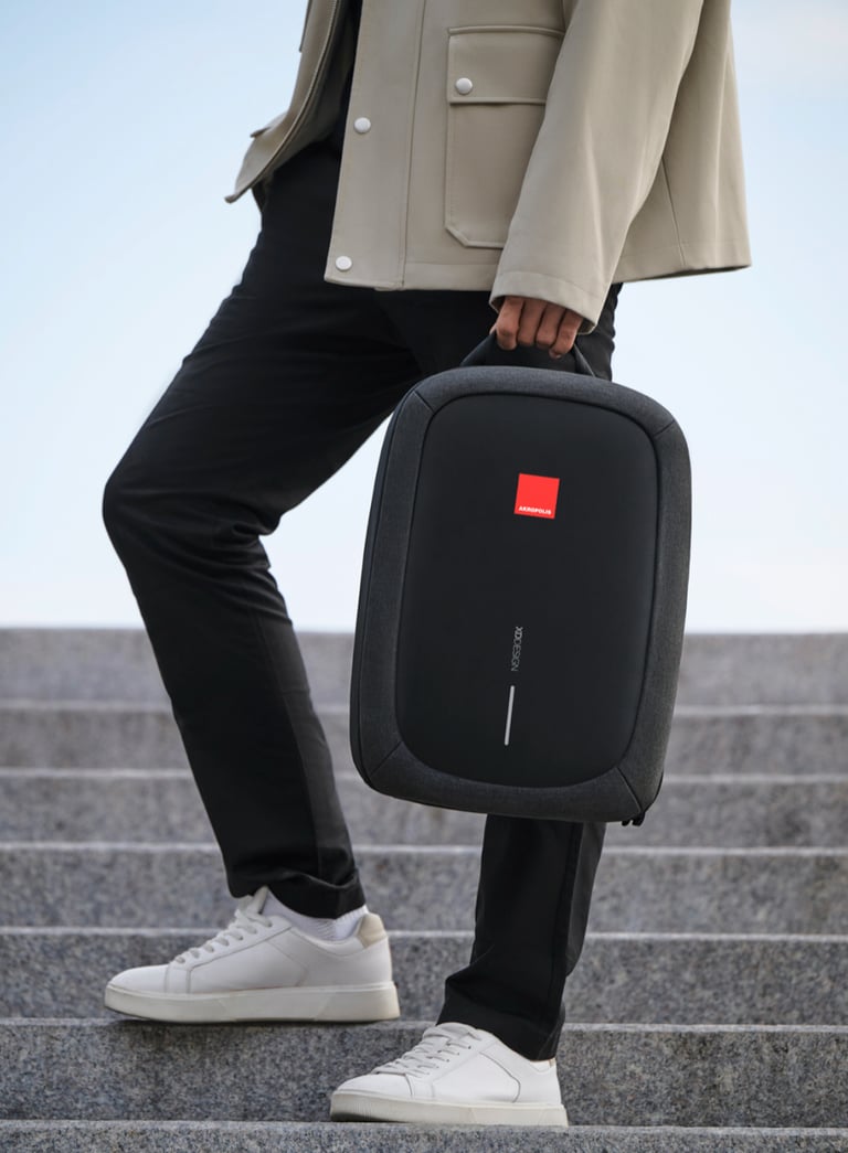 A man carrying a black XD Design anti-theft laptop bag while walking up stone stairs.