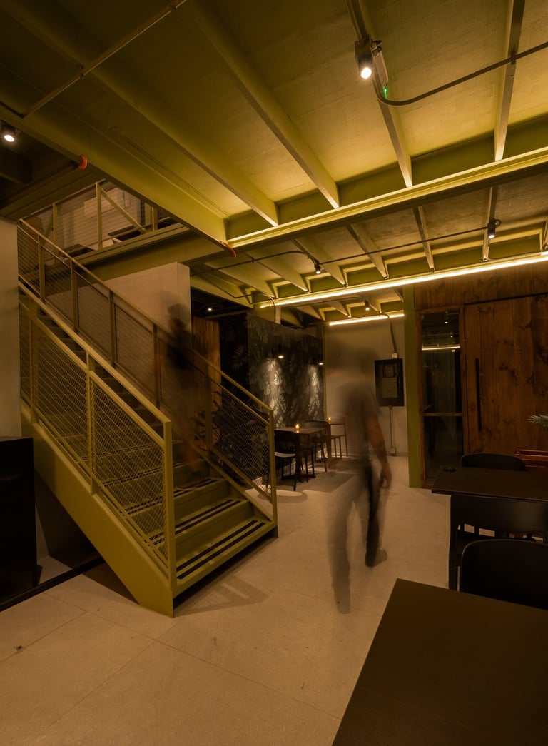 Un hombre caminando por un pasillo con una escalera, iluminacion indirecta.