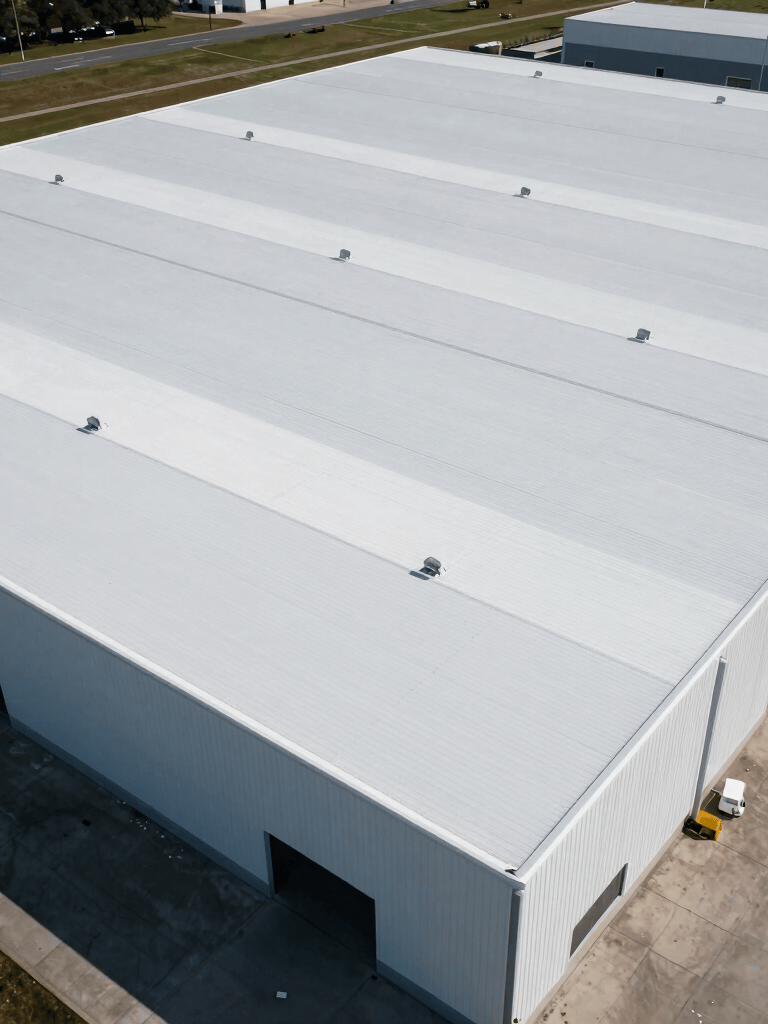 An aerial view of a massive North American warehouse featuring a pristine new white thermoplastic roof. The composition is clean and symmetric, emphasizing industrial scale and expert installation. Professional lighting highlights the smooth texture and durable quality.